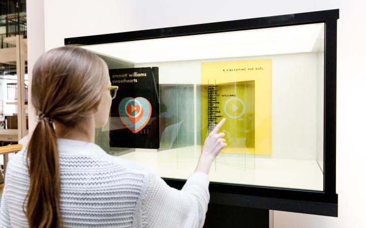 A woman stands in front of a glass box in which she can select and read books with her fingers.