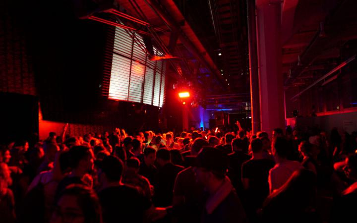 Das Foto zeigt den Gang des ZKMs in Richtung HfG in einem tiefen rot erleuchtet mit vielen tanzenden Menschen, die wie ein großer Körper durch das verschwommene Licht wirken.
