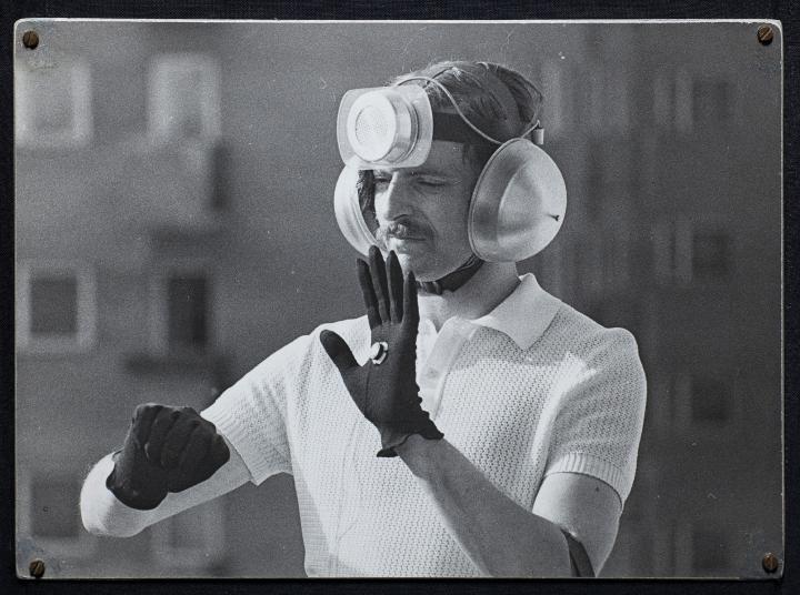 The black and white photo shows a man with a technical installation on his head, his ears covered with sound barriers.