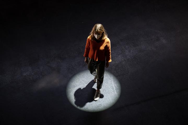 You can see a woman walking across a black floor, illuminated by a circular spotlight. 