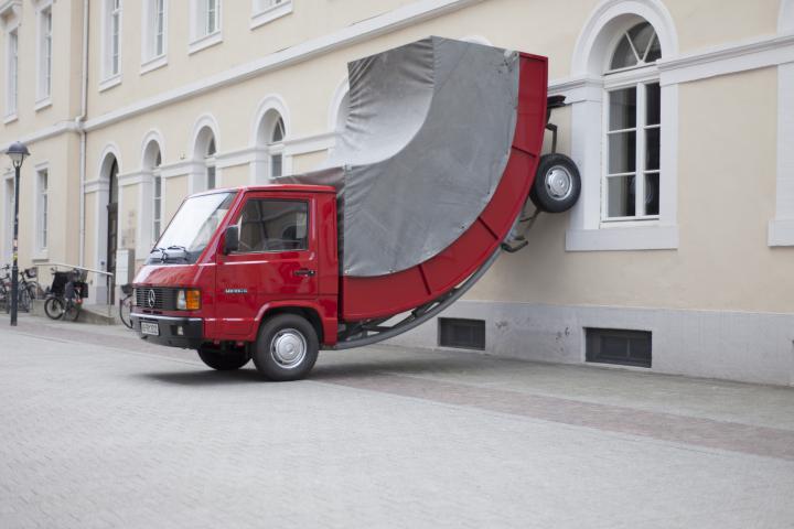 A red truck whose rear wheels stand at the wall
