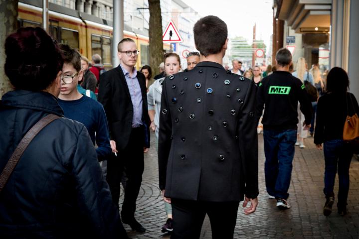 A Man wears a Jacket with some Camera-objectives in it