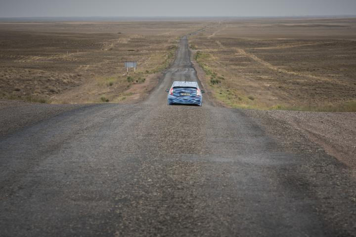A blue car driving through a desert landscapes