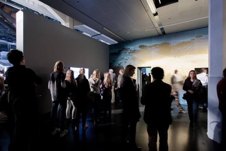 Many people standing in a room, looking at the artworks