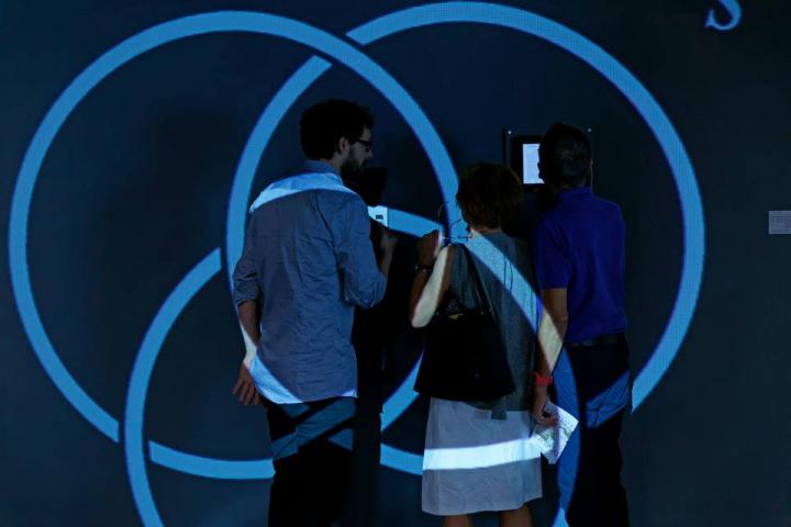 Three people standing in front of a wall. Blue circles are projected on them