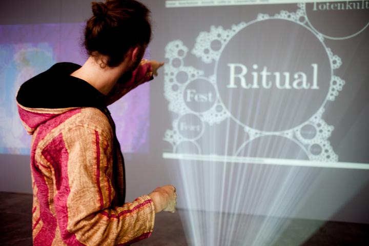A person in front of a projection on which "Ritual" stands