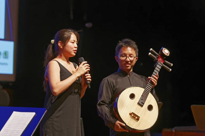 A woman with a microphone and a man with a kind of guitar