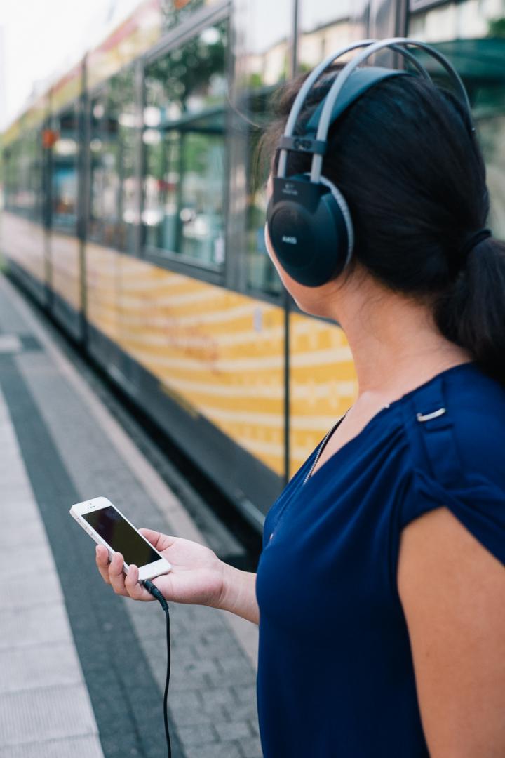 A woman with headphones and mobile in front of a tram