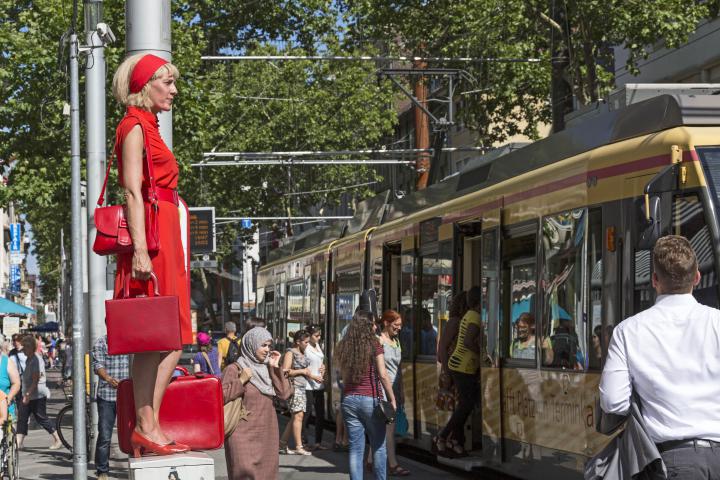 Eine Frau in Rot steht auf einem Stromkasten mitten in der Fußgängerzone