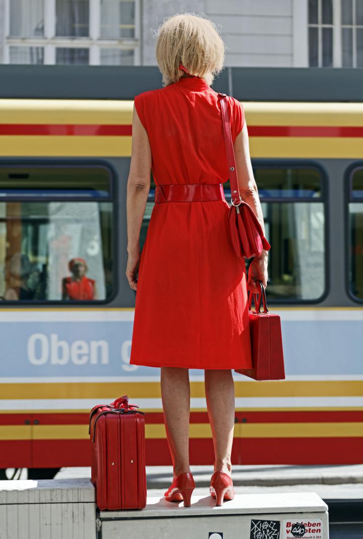 Eine Frau in Rot steht auf einem Stromkasten mitten in der Fußgängerzone