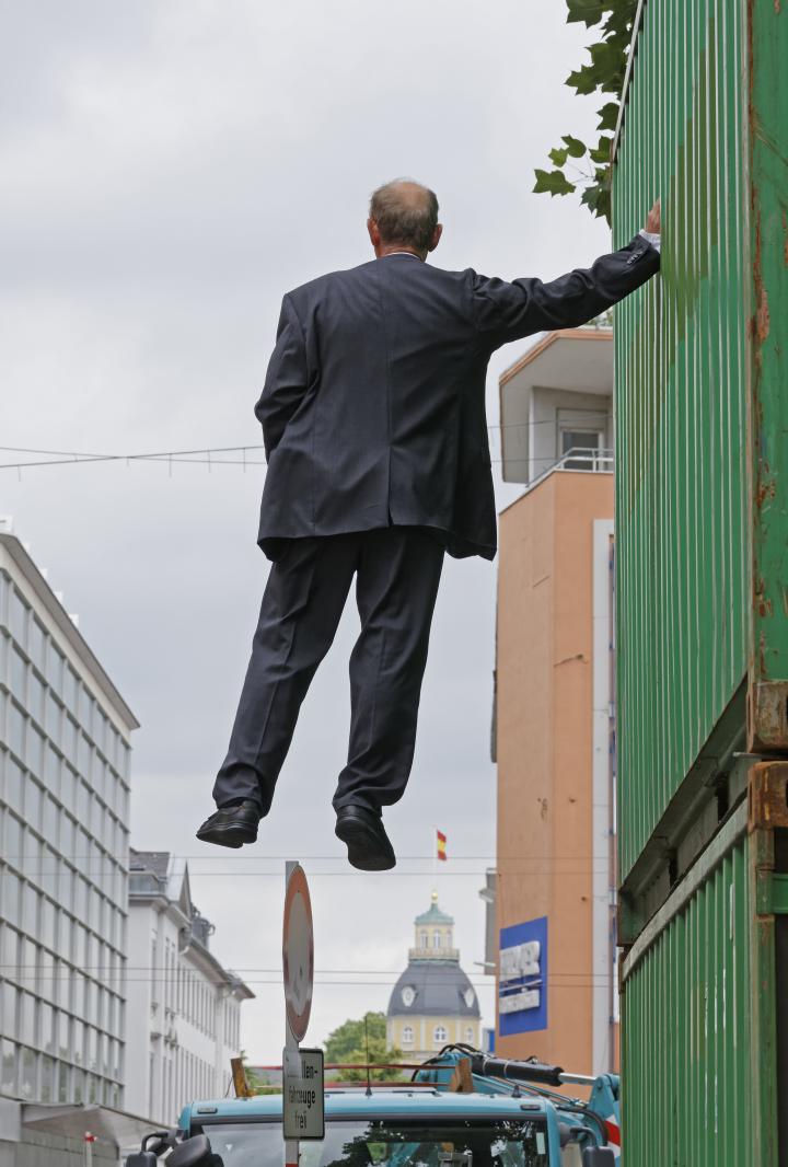 Ein Mann hängt in der Luft, hebt sich an einem Baucontainer mit nur einer Hand fest