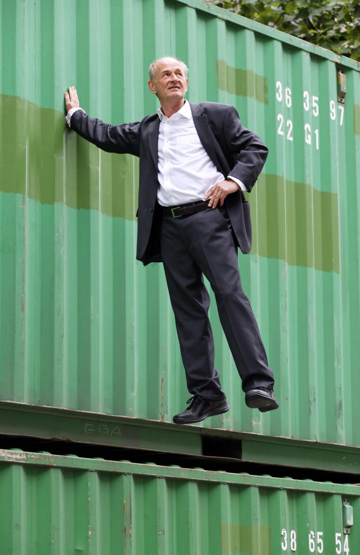Ein Mann hängt in der Luft, hebt sich an einem Baucontainer mit nur einer Hand fest