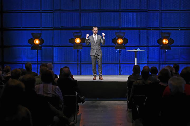 A man in a suit, standing on a stage.