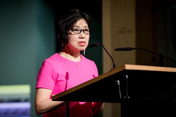 Eine Frau in pinkfarbenen Kleid spricht zum Publikum