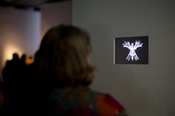 Eine Frau steht vor einem kleinen Bildschirm auf dem ein abstrakter, leuchtender Schmetterling zu sehen ist
