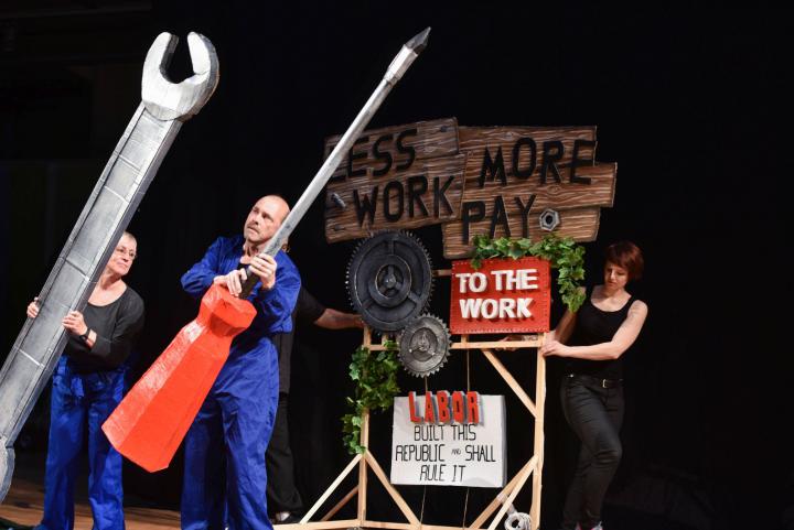 Three people fiddling with oversized tools made of paper mache