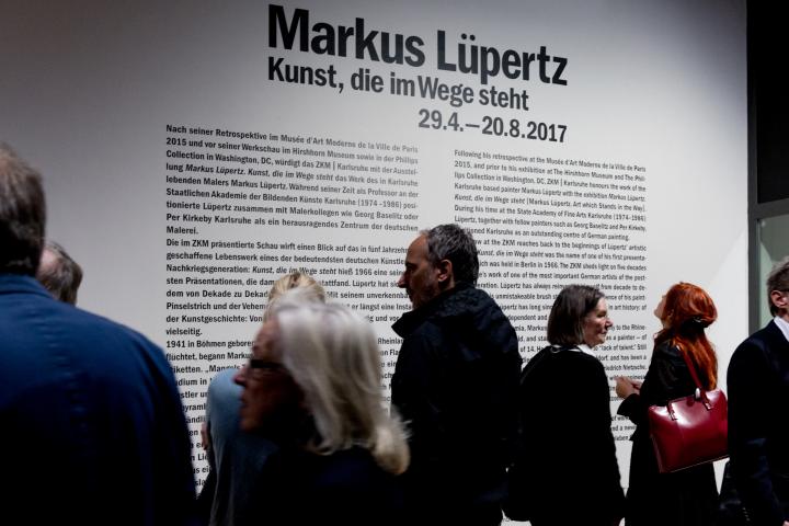 The picture shows visitors in front of an information board for Markus Lüpertz