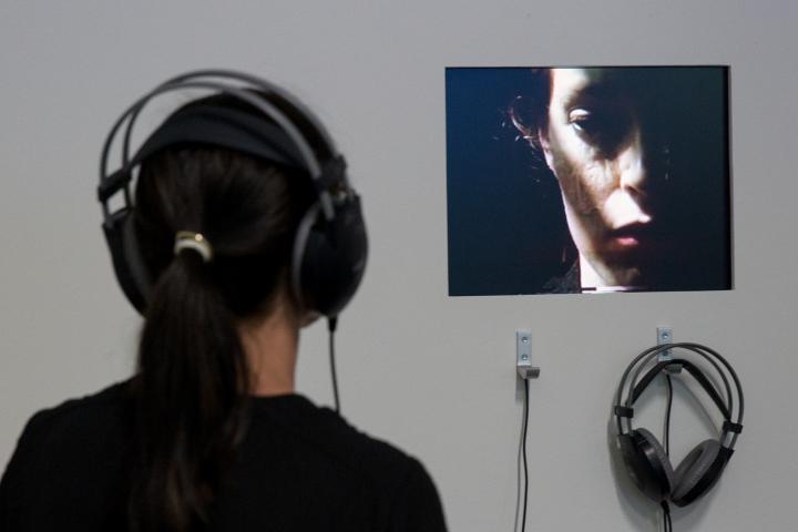 A woman with headphones is watching a video of another woman.