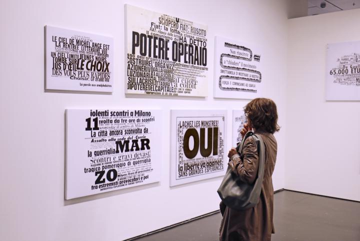  The picture shows the back of a woman looking at the collages of the artist Nanni Balestrini.