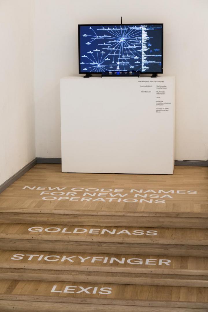 Installation with a screen and white text on the floor in front of it