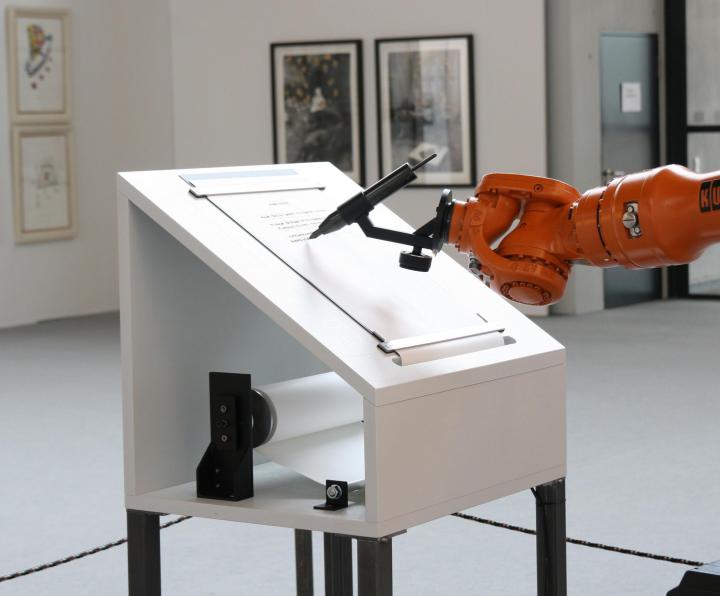 Das Bild zeigt einen Roboterarm, der ein Manifest verfasst