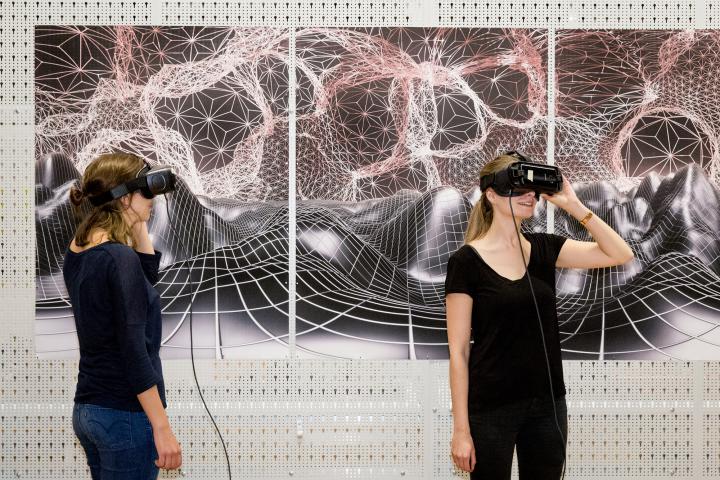 Zwei Frauen mit VR-Brillen stehen vor einer graphischen Landschaft