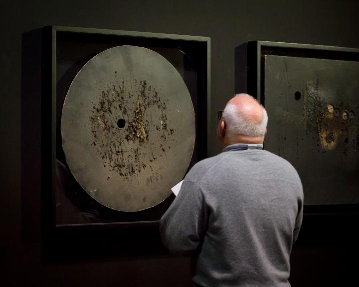 Das Foto zeigt den Rücken eines glatzköpfigen Mannes vor einem Werk von Aldo Tambellini. 