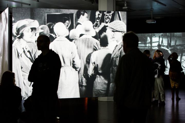 The photo shows the exhibition room with a large projection of a black and white film.