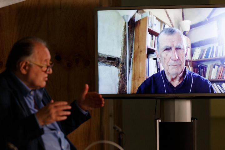Peter Weibel sitzt vor einem großen Bildschirm auf dem Bruno Latour zu sehen ist.
