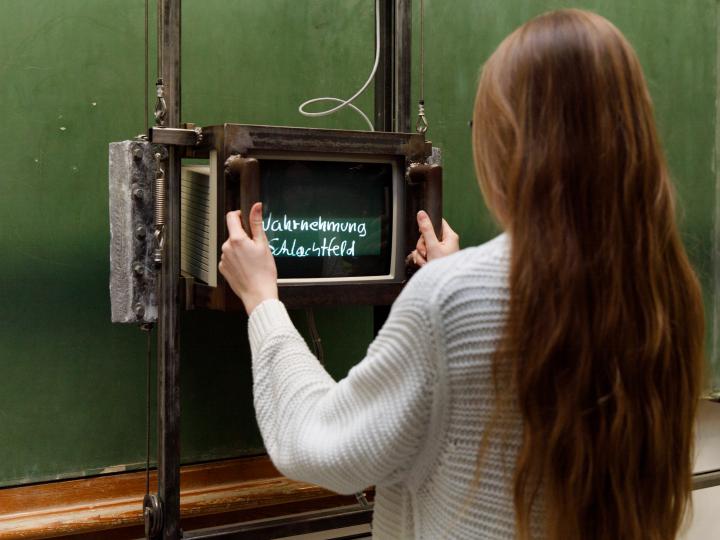 Besucherin vor Fietzeks »Tafel«, eine leere grüne Schultafel, auf der mit Hilfe eines Monitors zuvor unsichtbare Texte auftauchen.