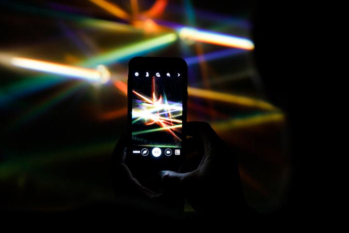 A smartphone in camera mode photographs the beams of colorful light prisms.