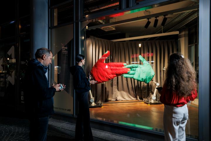 On the picture you can see the instalation "Handshake", AATB (Andrea Anner, Thibault Brevet), in the triangle at Kronenplatz. A big ror and big green hand are fixed on the ground and hit each other. Several people are standing in front of the window.