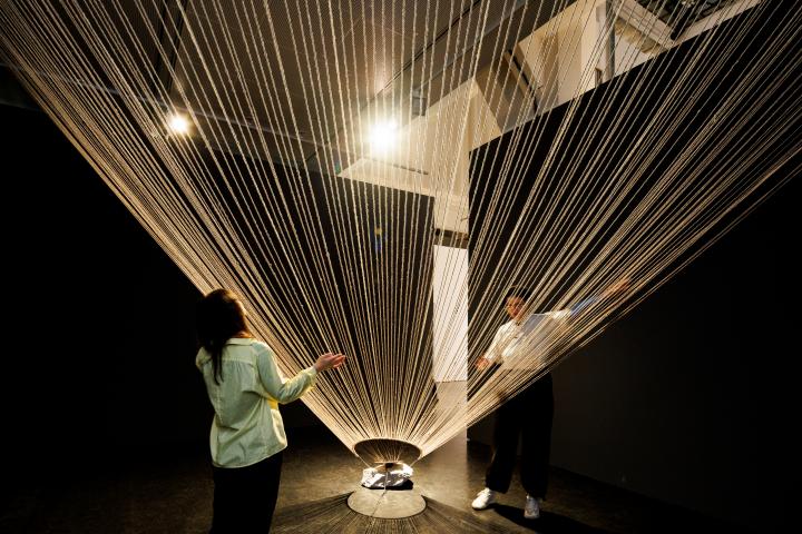You can see a ceiling-high, wide net made of ropes. Two people are standing next to it, one on the left and one on the right.