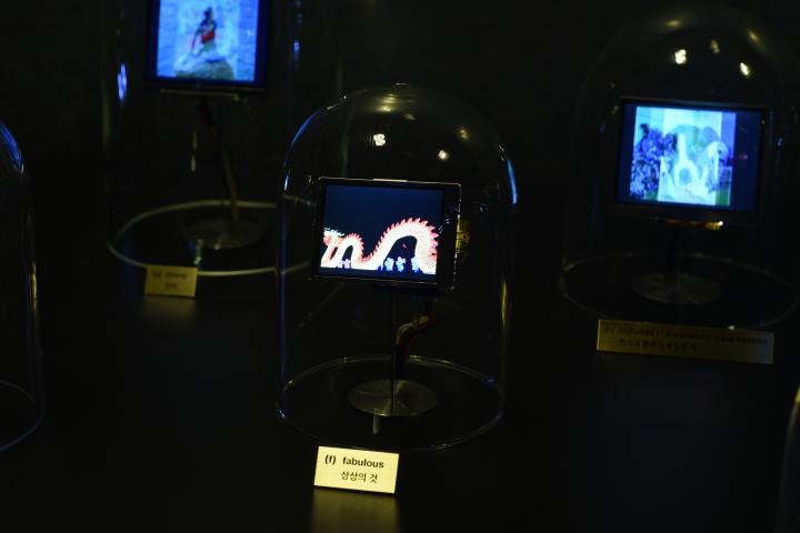 Das Foto zeigt eine Glasglocke in der ein kleiner Bildschirm steckt. Auf diesem ist ein Drachen ähnliches Wesen zu sehen.