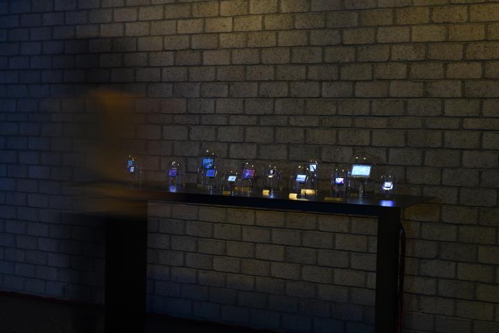The photo shows a dark table with several glass bells with integrated displays are exposed. A person is blurred on the left side.