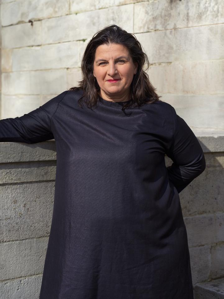 Portrait von Çağla Ilk in schwarzem Kleid vor einer weißen Steinmauer 