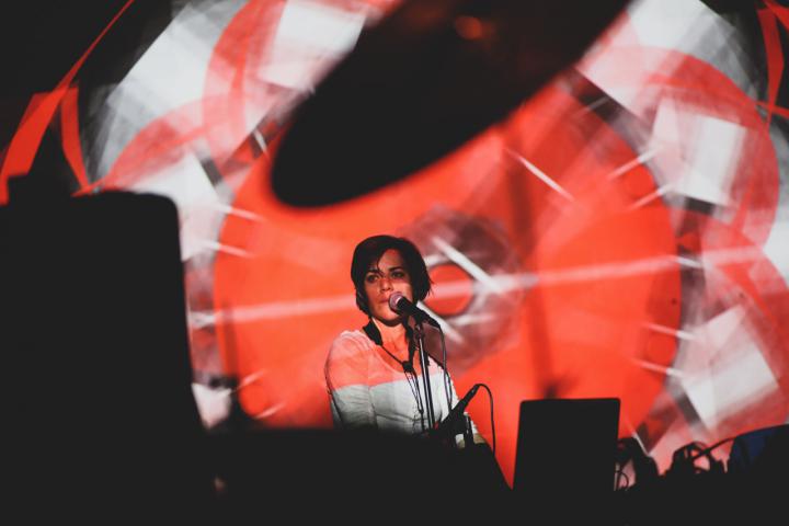Eine Frau am Mikrofon, vor ihr rot-weiße Lichtprojektionen.