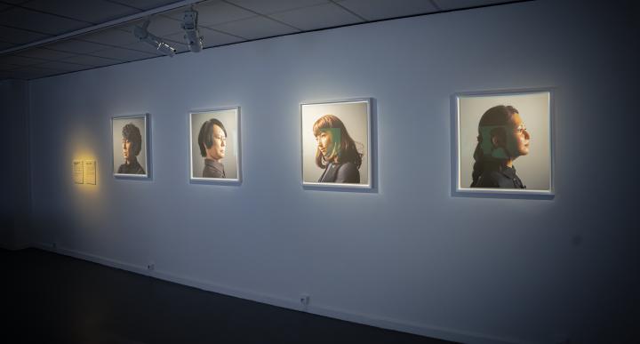 Zu sehen sind vier Porträts, die unterschiedliche Menschen abbilden, an einer Wand. 