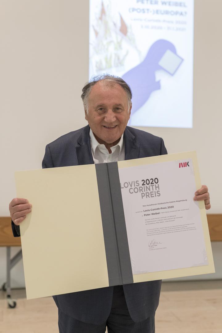 Ein Foto des Künstlers, Kurators und ZKM-Vorstands Peter Weibel, der den Lovis-Corinth Preis in Form einer Urkunde in den Händen hält.