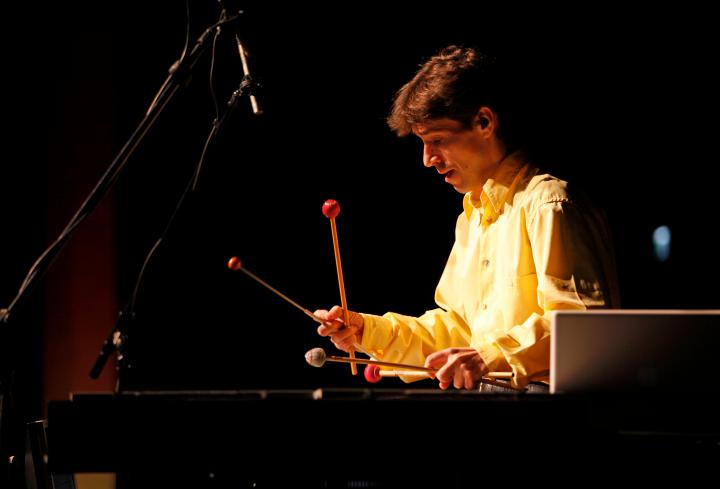 Ein Mann spielt mit gesenktem Bilck auf einem großen Xylophon mit vier Klöppeln von denen er jweils zwei überkreuzt in der Hand hält.