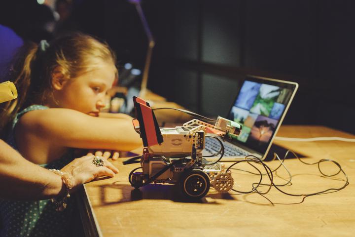 Ein Kind lehnt an einen Tisch, auf dem ein kleiner Roboter steht 