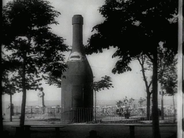 The screenshot shows a shaky black and white image of an oversized bottle surrounded by trees.