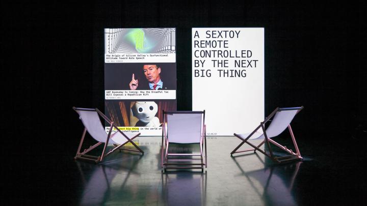 The photo shows three deck chairs in front of two upright rectangular canvases. On the left screen you can see a spiral form, the head of a man and the head of a robot. A text appears on the right screen. 