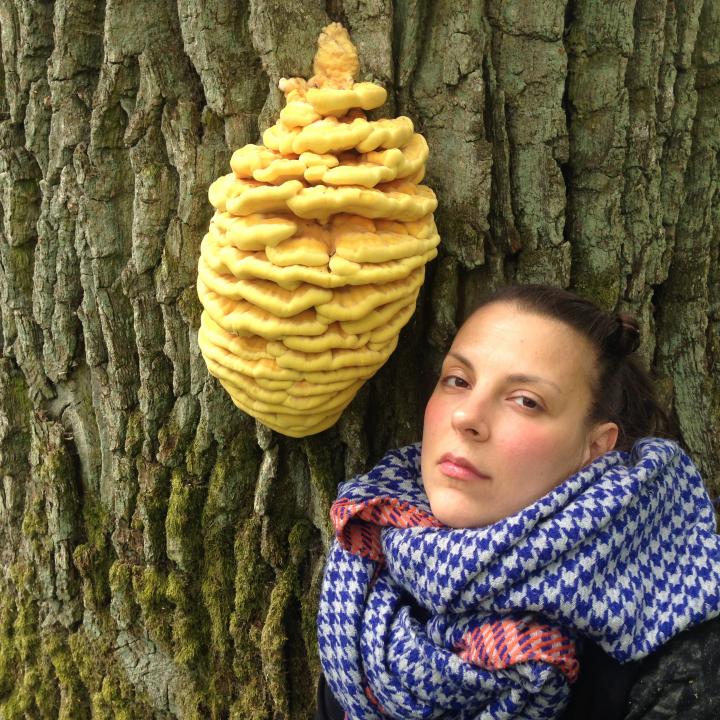 A woman with a blue and white checkered scarf poses next to a tree mushroom