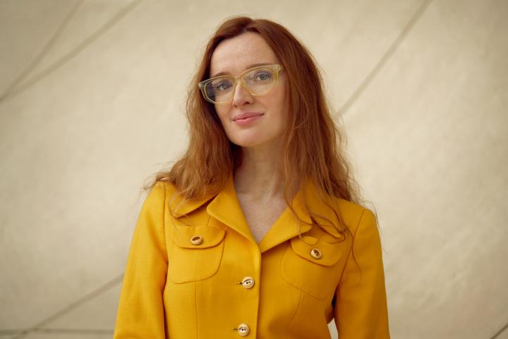 A woman with long red hair dressed in a yellow blouse.