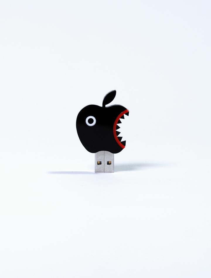 Das Foto zeigt einen USB Stick als schwarzer PacMan ähnlicher Apfel getarnt. 