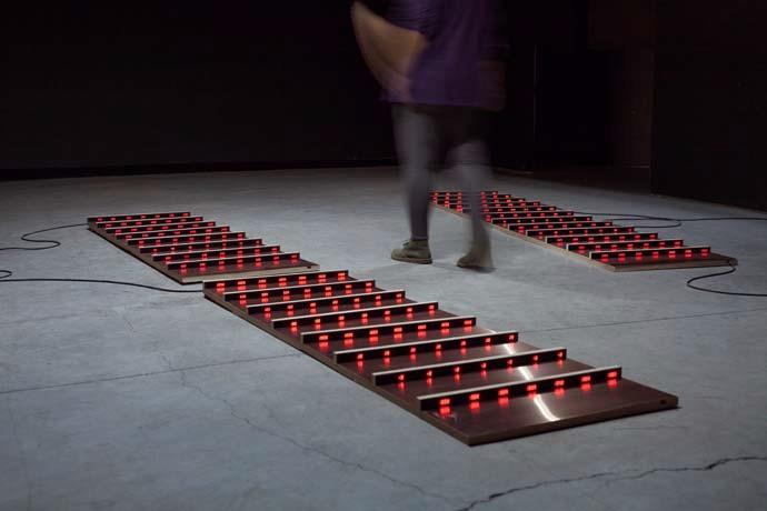 Exhibition view of the work »Patterns of Heat«, , plates lying on the floor with red luminous crossbars.