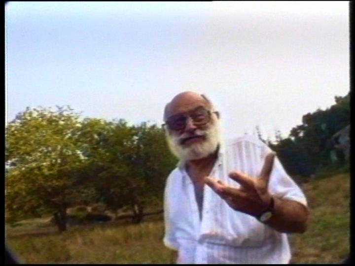 Mean with beard in a white shirt talks into the camera. It is Vilém Flusser