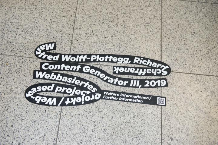 Auf einem gefließten Boden klebt die schwarze Schlaufe der Ausstellung »Seasons of Media Arts«, mit weißer Schrift über das Kunstwerk Content Generator III 