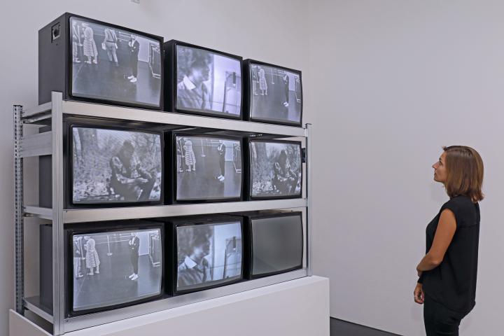 Besucherin vor einer Installation aus neun Fernsehbildschirmen, 